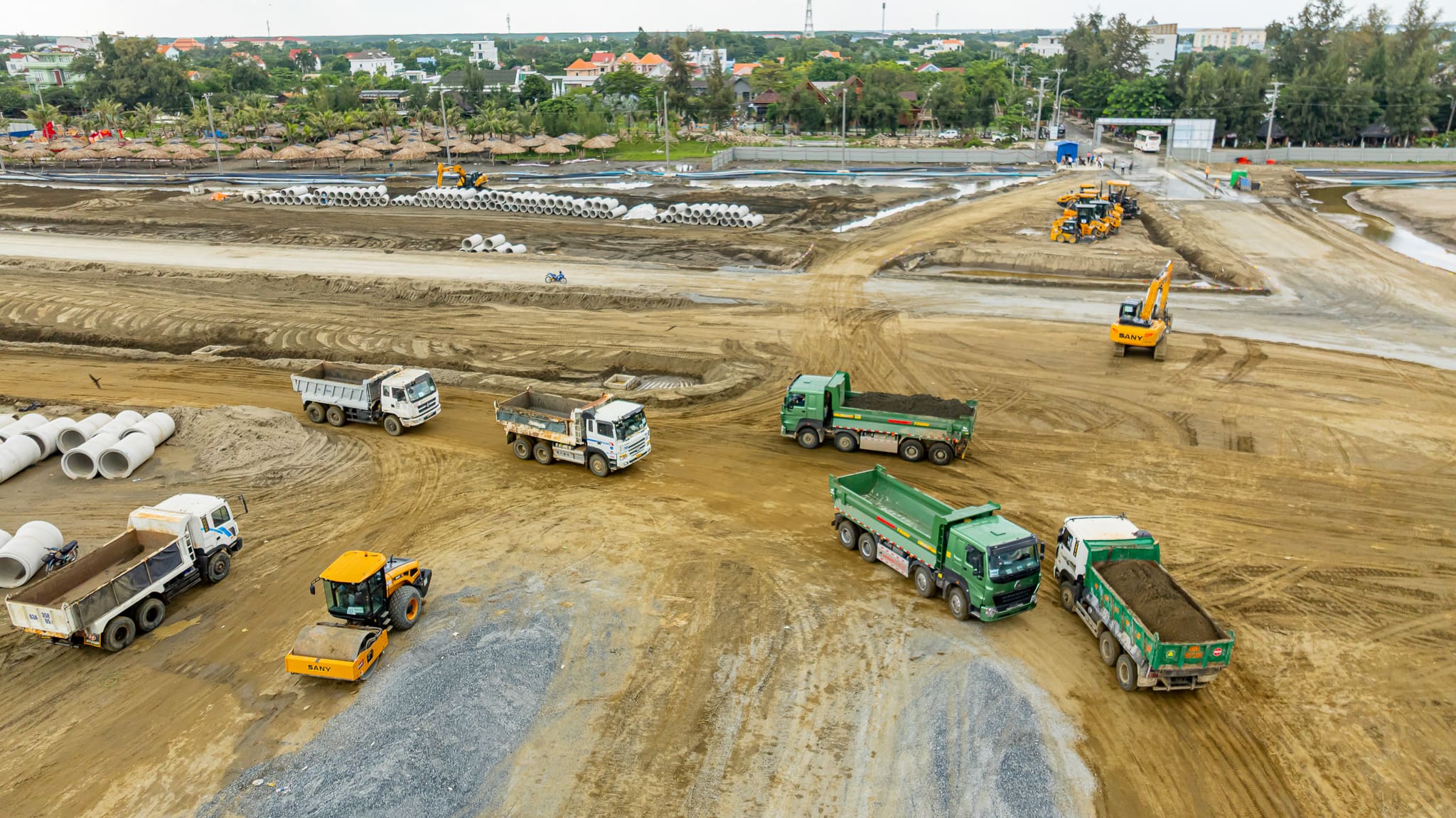 Bên trong công trường, ô tô nối đuôi nhau thành hàng vận chuyển vật liệu, tạo nhịp độ khẩn trương cho dự án.
